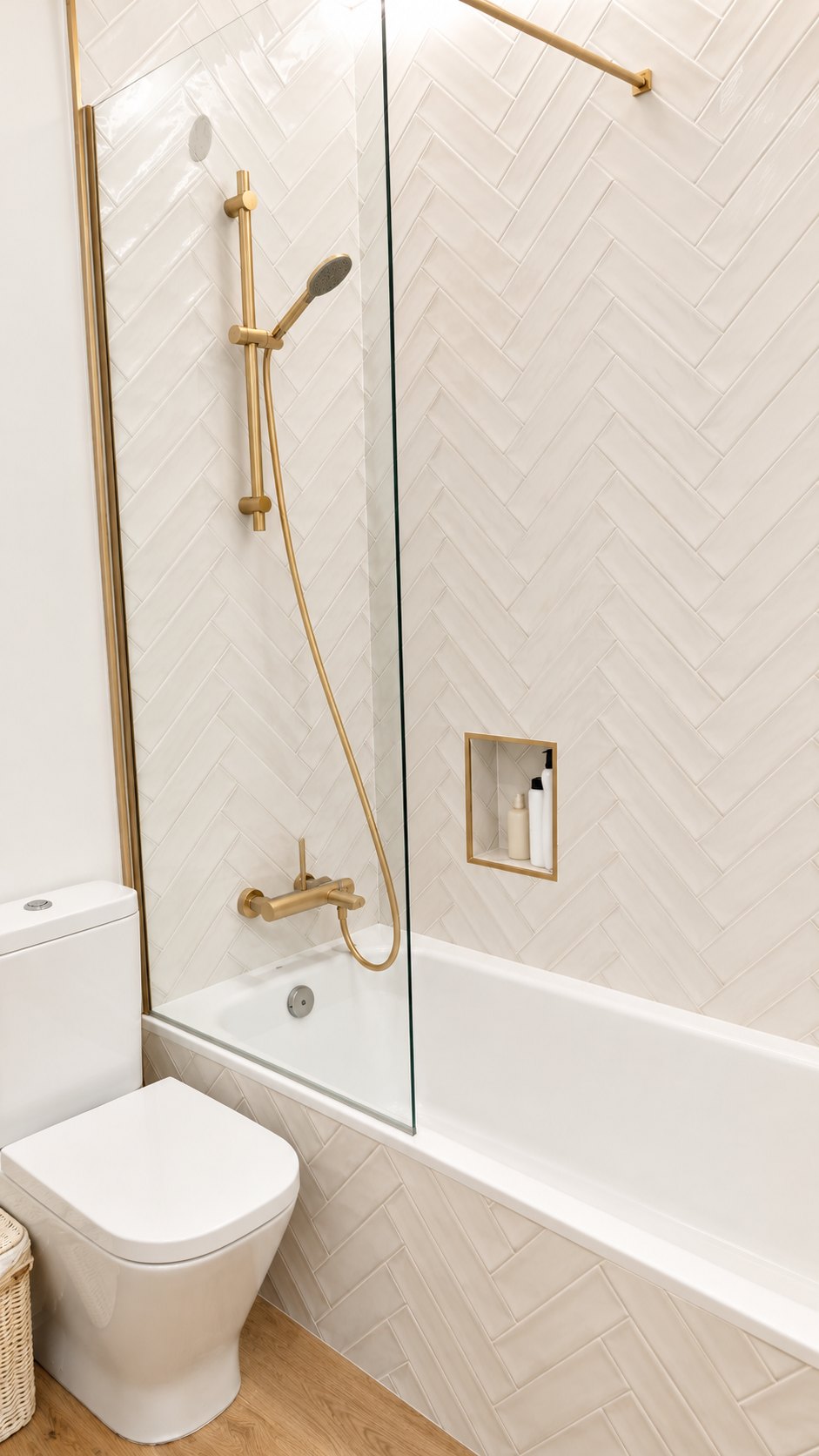 Baño con bañera, mampara de cristal y grifería dorada sobre azulejos en espiga