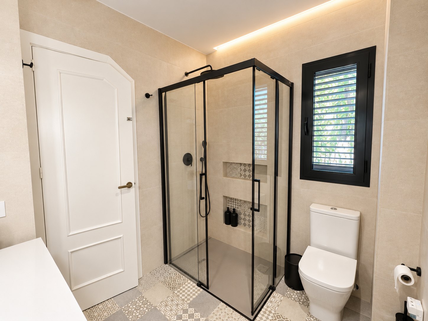 Baño con ducha de cristal y perfiles negros, hornacinas de mosaico y ventana con lamas