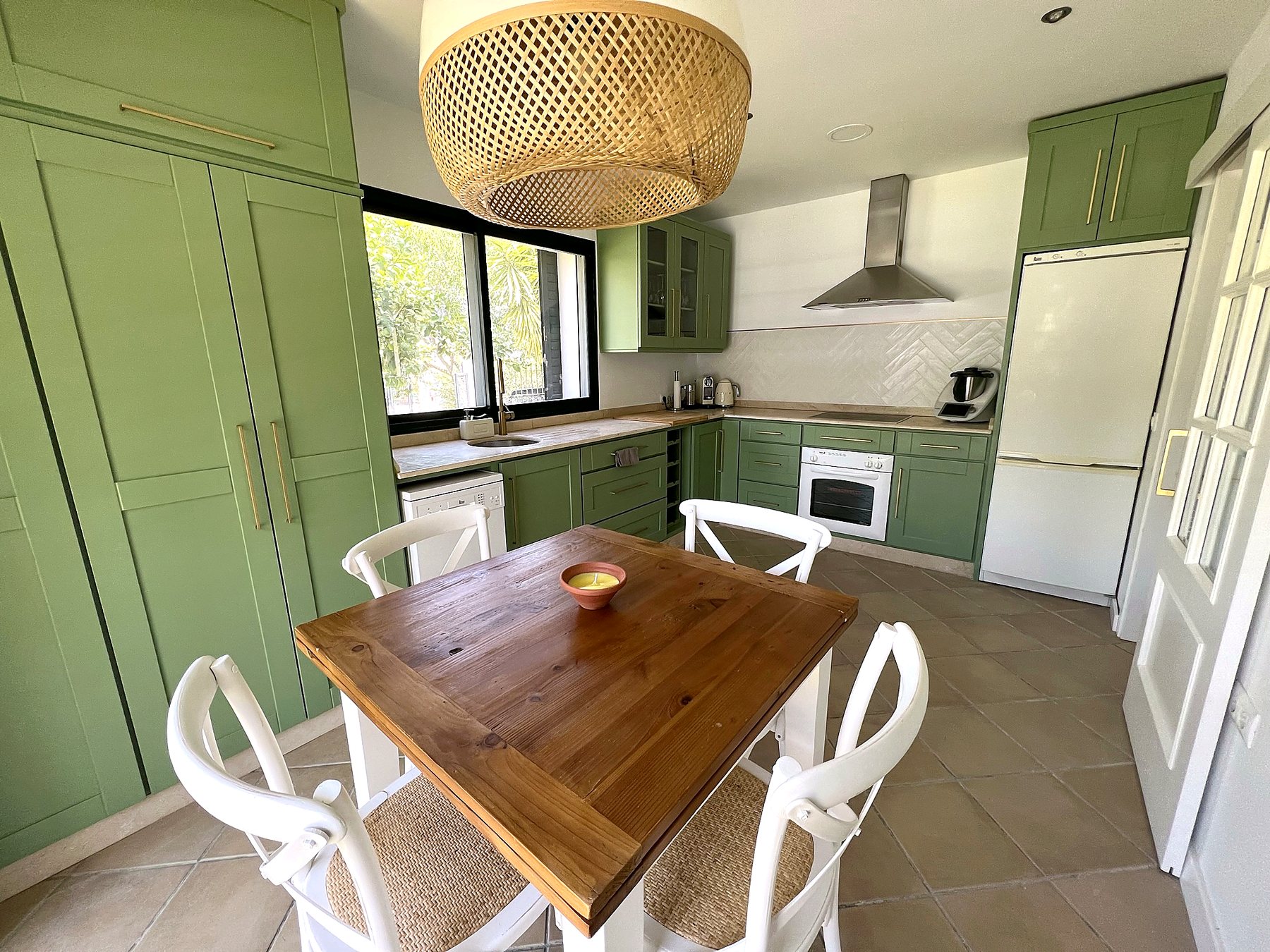 Mesa de comedor de madera con sillas blancas y la cocina al fondo