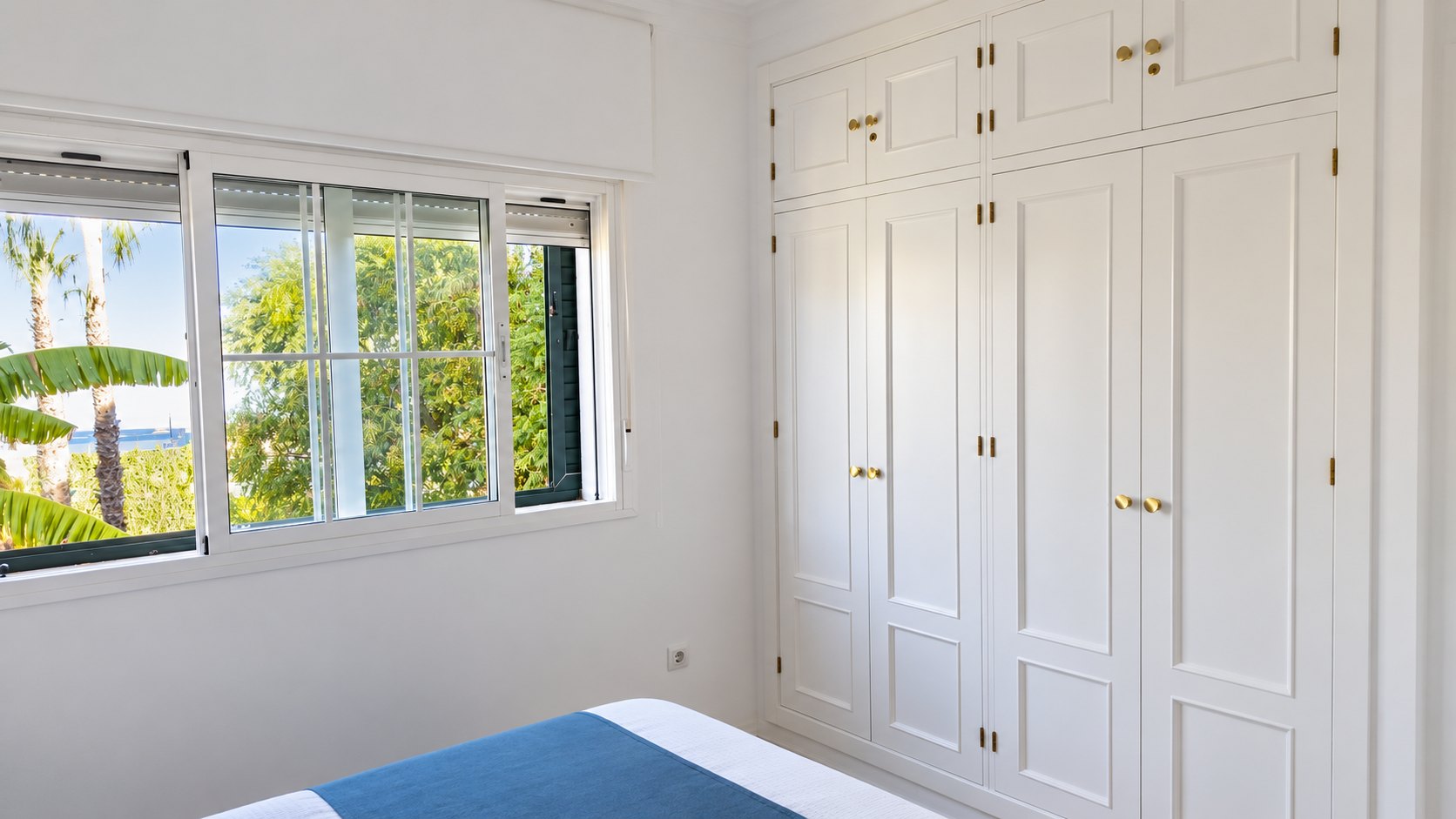 Dormitorio con armarios blancos empotrados y ventana al jardín