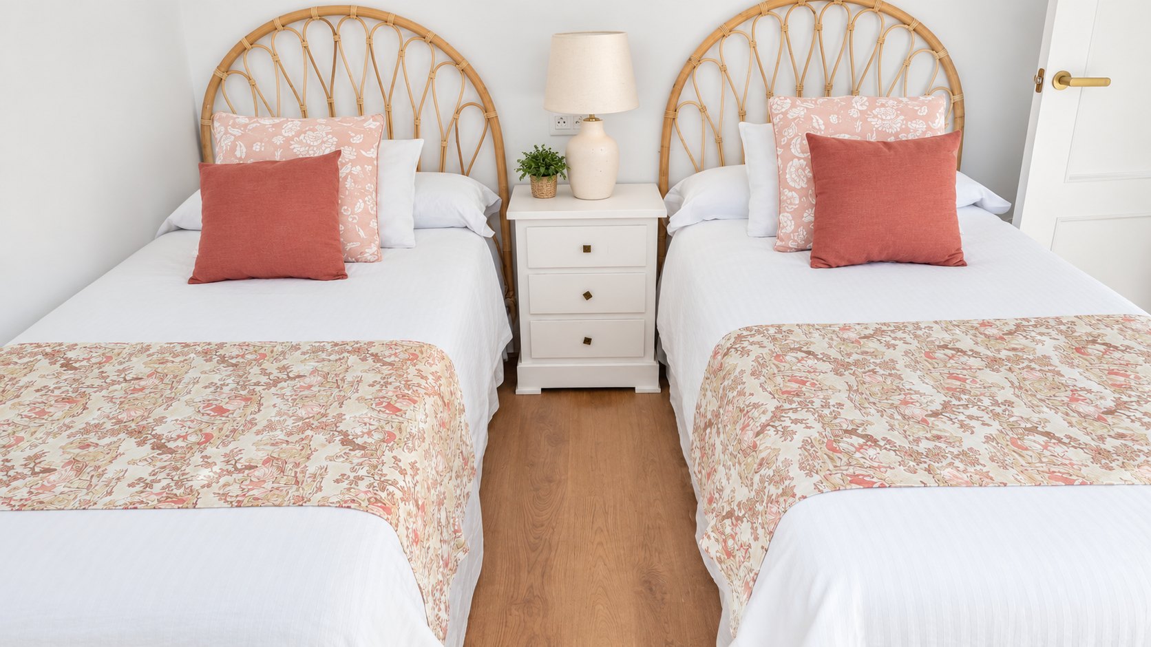 Dormitorio con dos camas individuales, cabeceros de ratán y cojines coral