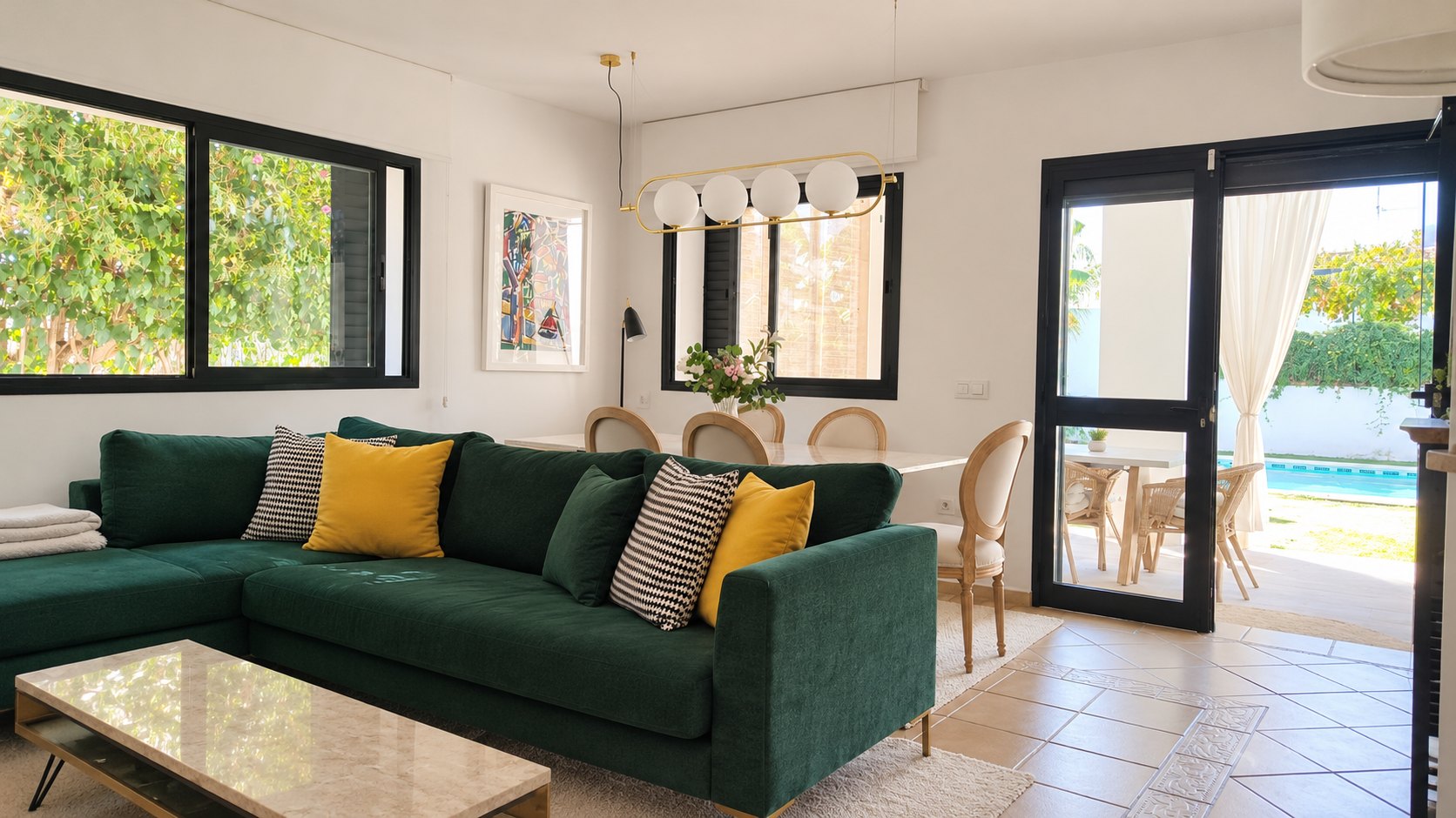 Salón con sofá verde, comedor de mármol y puerta abierta a la piscina